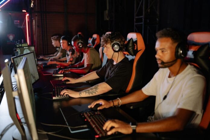Młodzi gracze e-sportowi rywalizują przy komputerach w hali turniejowej